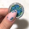 Un pot rempli de pétales de fleurs séchées dans des nuances pastel vert et turquoise - Semilac Flower Flakes Spring Meadow. Un ongle avec un vsp rose tendre est décoré de quelques pétales.