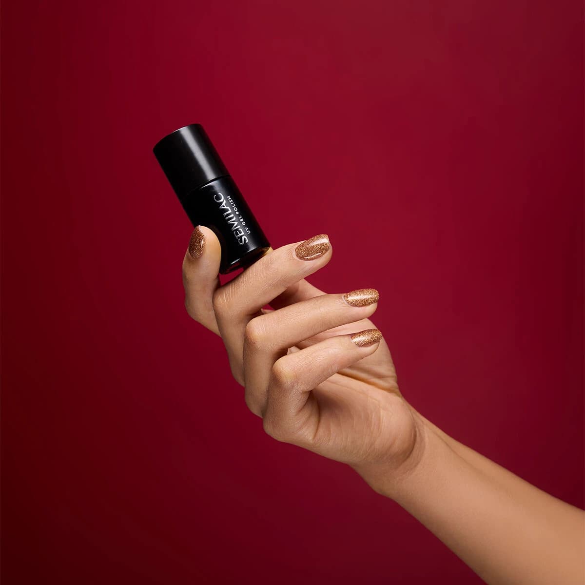 Main qui tient le flacon du du Semilac – Vernis semi-permanent 956 Vintage Gold. Sur les ongles un doré intense et holographique.
